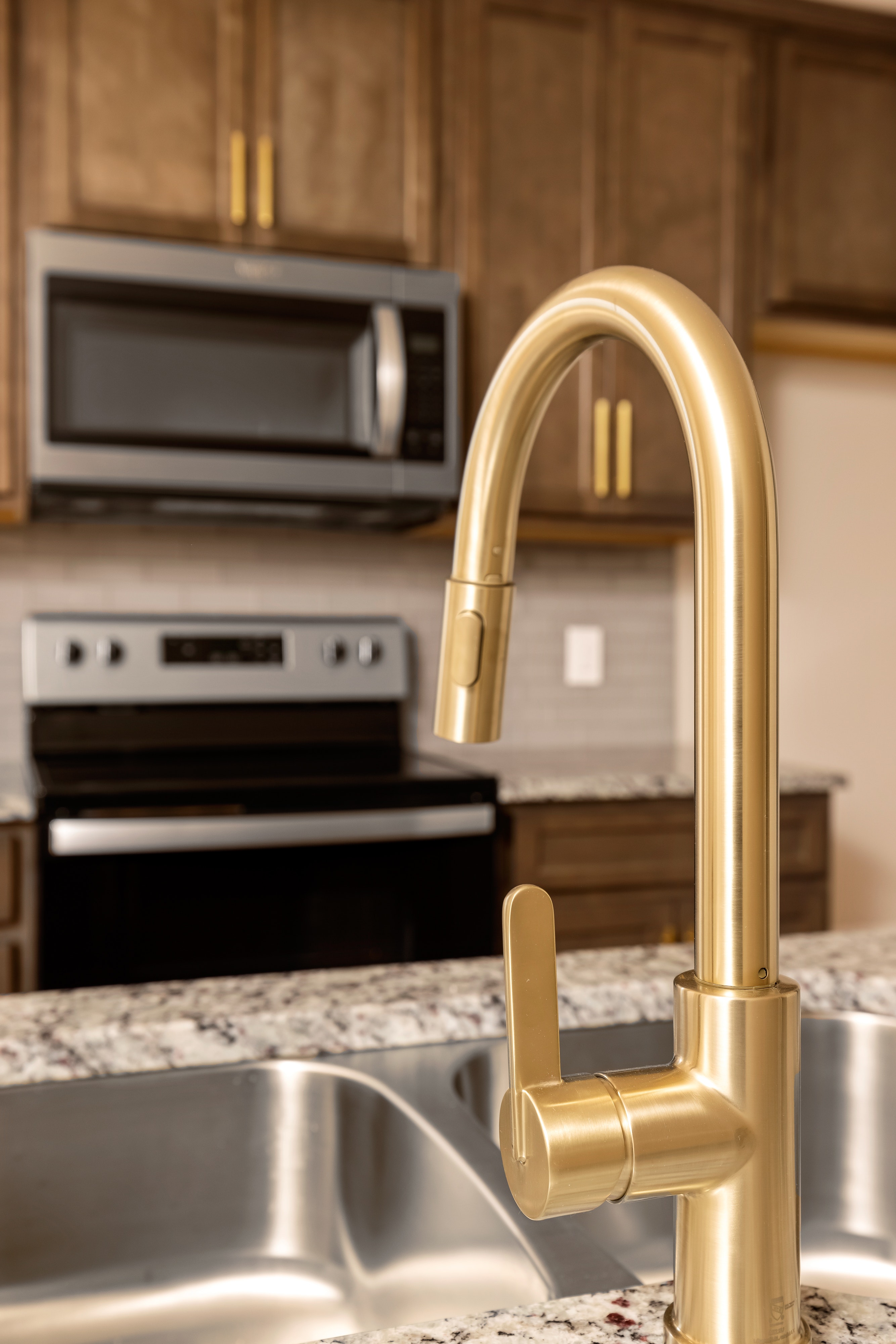 a kitchen view from the sink with a gold faucet and stove in the background