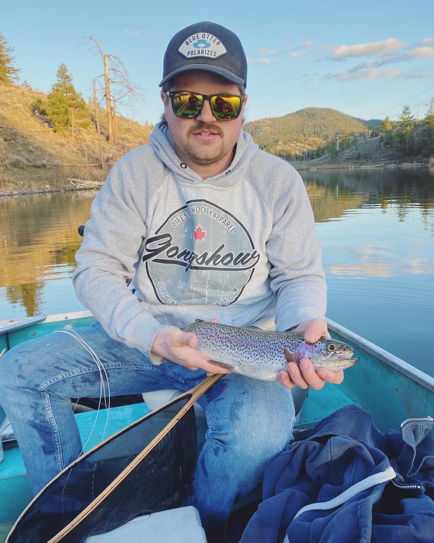man in fishing boat wearing a hat and sunglasses holding a fish in his hand floating on the water