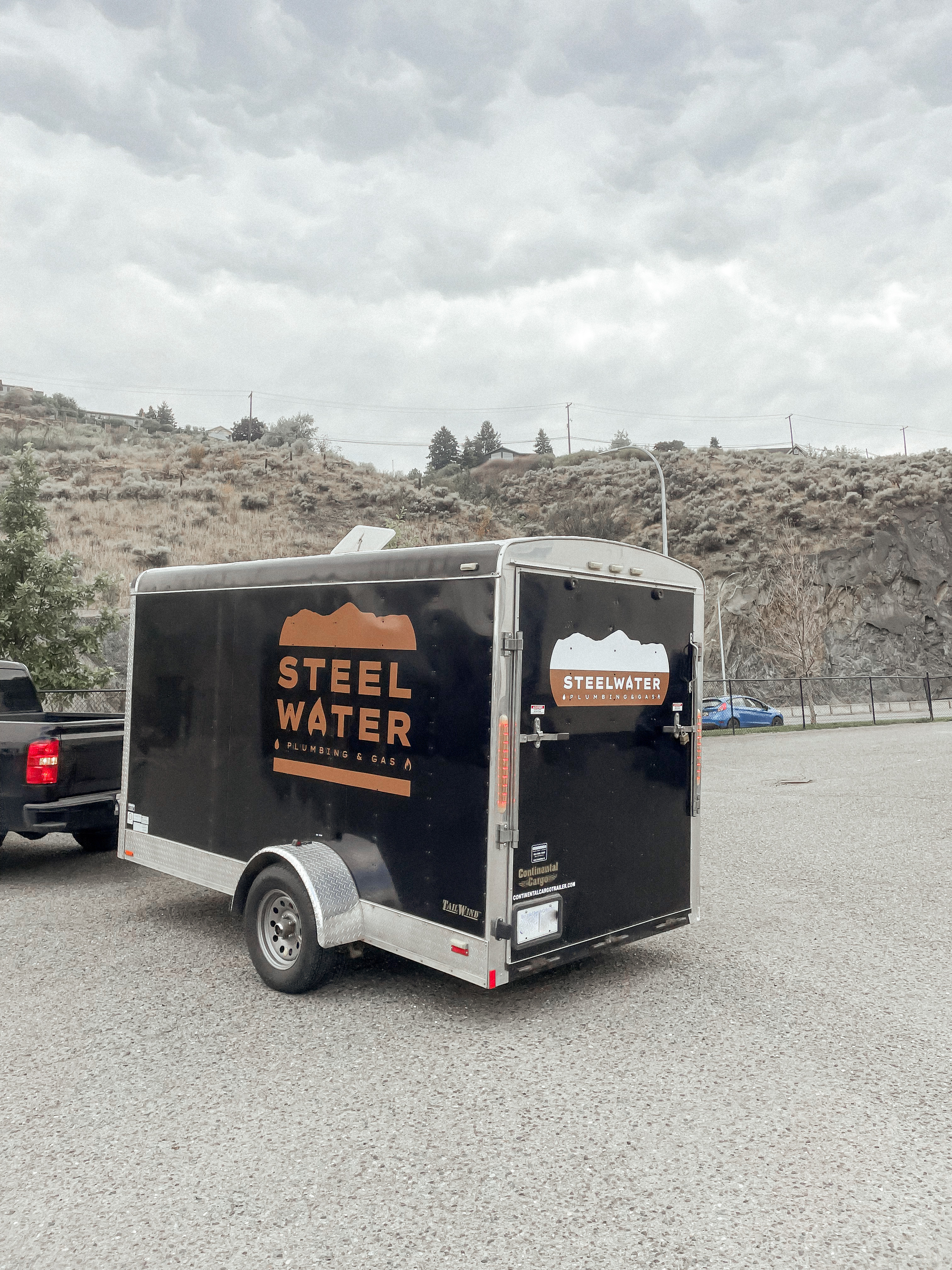 Black utility trailer and black truck representing Steelwater Plumbing & Gas Ltd. with logo on side of trailer.